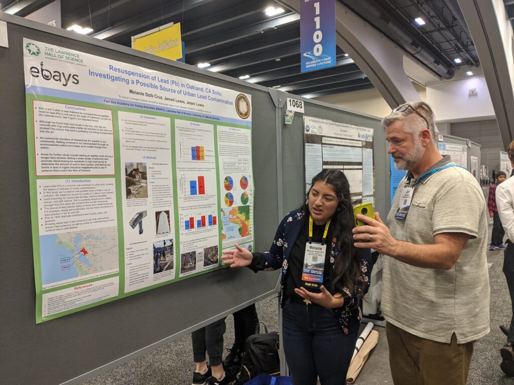 EBAYS youth gesturing at their scientific poster showing the results of their study while an adult listens